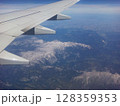 A stunning vista reveals snow-capped mountain ranges and lush valleys as seen from an airplane window during a clear daytime flight. The scene captures the vastness of nature. 128359353