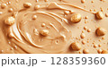 Swirls of creamy peanut butter highlight the smooth texture with scattered whole peanuts and tiny droplets glistening. This appealing arrangement showcases the richness of the spread. 128359360