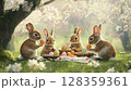 Four adorable rabbits are engaged in an Easter egg celebration in a lush garden. They are sitting on the grass, carefully holding colorful eggs as cherry blossoms surround them. 128359361