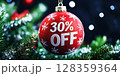 A vibrant red ornament hangs from a fir tree, displaying a 30 off offer. Surrounding lights create a festive atmosphere, embodying the spirit of holiday shopping. 128359364
