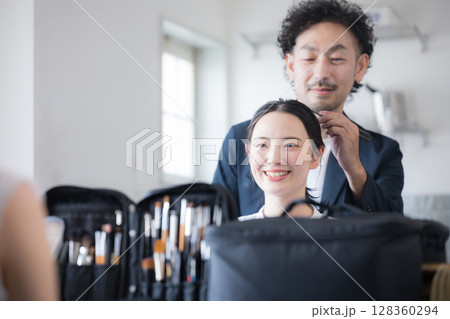 メイクブラシを持つヘアメイクの男性と女性　メイクアップのイメージ　鏡を見る	 128360294