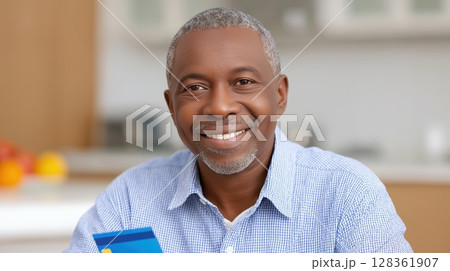 Social security benefits concept, Smiling man holding a credit card in a bright kitchen setting. 128361907