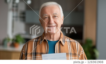 Social security benefits concept, Smiling elderly man holding documents in a cozy indoor setting. 128361908