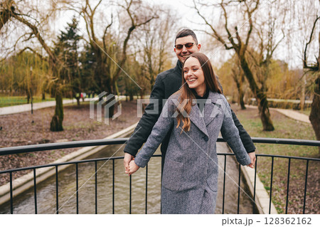 Couple enjoys a joyful moment together on a bridge in a park surrounded by trees in early spring 128362162