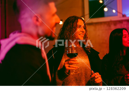 Friends enjoying an evening gathering with drinks and laughter in a cozy outdoor setting during nighttime 128362209
