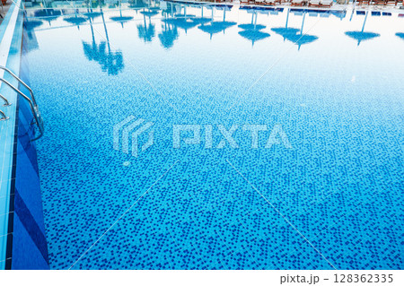 Bright blue swimming pool reflecting palm trees in sunny outdoor setting 128362335