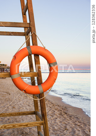 Lifebuoy hanging from wooden lifeguard stand near calm beach at sunset 128362336