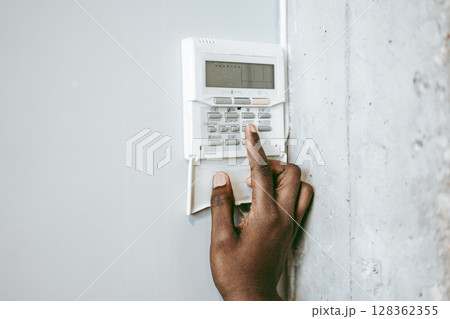 Person interacting with a security panel on a wall in a modern setting during daytime 128362355