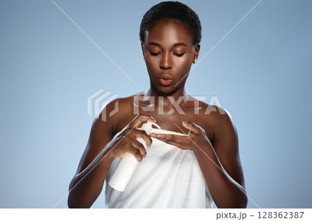 Woman applying skincare product while wrapped in towel in bright studio setting 128362387