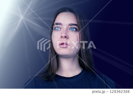 Woman with blue eyes gazing thoughtfully against a dark background in an artistic light setting Woman with blue eyes gazing thoughtfully against a dark background in an artistic light setting 128362388