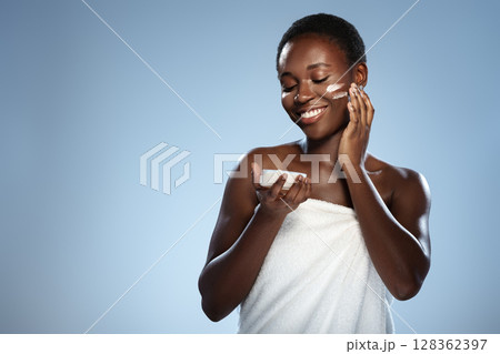Young woman applying skincare product while smiling in a bright setting during the day Young woman applying skincare product while smiling in a bright setting during the day 128362397