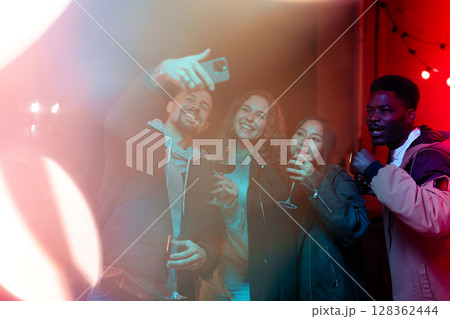 Friends enjoying a night out, taking selfies, and celebrating a special occasion at a lively venue with colorful lights Friends enjoying a night out, taking selfies, and celebrating a special occasion at a lively venue with colorful lights 128362444