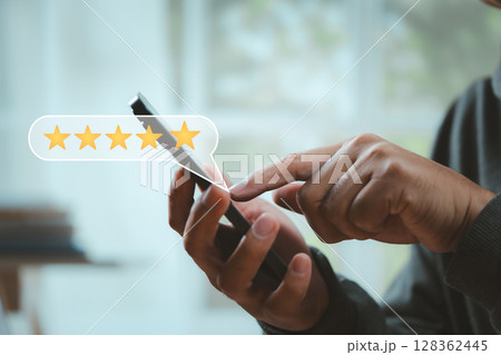 Close-up of hands giving a five-star rating on smartphone screen. Concept of online review, user experience, digital reputation, and customer satisfaction. 128362445