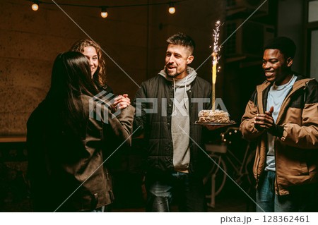 Friends celebrate a birthday with cake and laughter during an evening gathering at a cozy venue 128362461