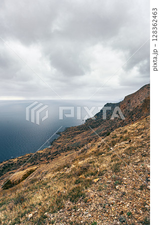 Coastal landscape with rugged cliffs and deep blue ocean under cloudy sky Coastal landscape with rugged cliffs and deep blue ocean under cloudy sky 128362463