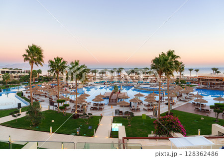 Luxurious resort pool area at sunset with palm trees and loungers near the beach Luxurious resort pool area at sunset with palm trees and loungers near the beach 128362486