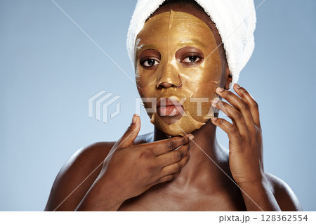 Woman applying gold face mask at home for skincare routine while wearing a towel on her head Woman applying gold face mask at home for skincare routine while wearing a towel on her head 128362554