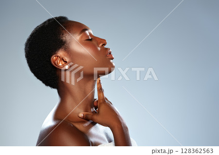 Elegant woman showcases beauty with poised expression and gentle hand on her neck against a soft blue background 128362563