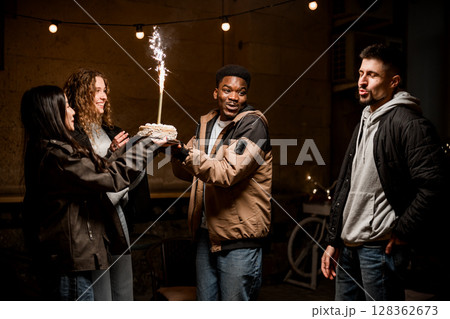 Joyful celebration with friends and cake featuring a sparkling candle during an evening gathering 128362673
