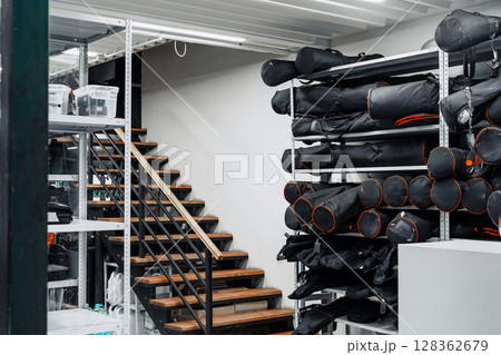 Storage area showing neatly organized black gear bags on shelves with wooden stairs in a well-lit space Storage area showing neatly organized black gear bags on shelves with wooden stairs in a well-lit space 128362679