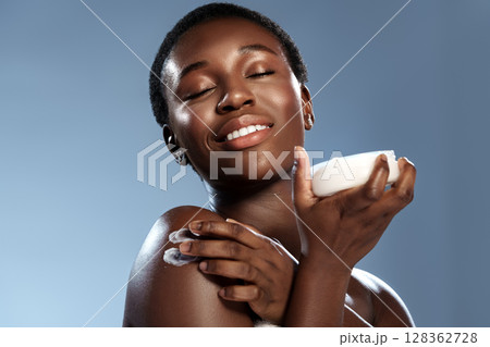 Woman enjoying self-care with body lotion against a soft blue background during a beauty routine 128362728