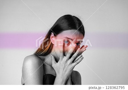 Portrait of a woman expressing emotion with hands covering her face in a minimalist setting during daylight 128362795
