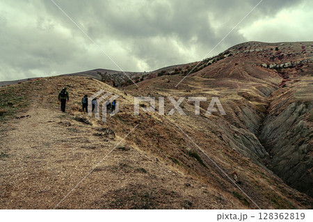 Hikers traverse rugged terrain under cloudy skies in a remote landscape during late afternoon 128362819