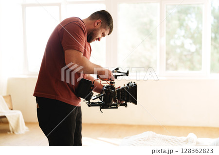 Filmmaker adjusting camera equipment in a bright studio during a creative session Filmmaker adjusting camera equipment in a bright studio during a creative session 128362823