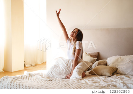 Morning routine of a woman waking up and stretching in a cozy bedroom with natural light pouring in 128362896