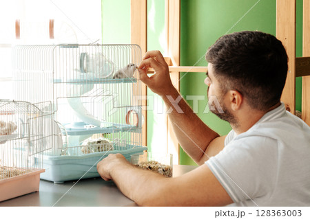 Man interacting with small birds in a cage during afternoon at home 128363003
