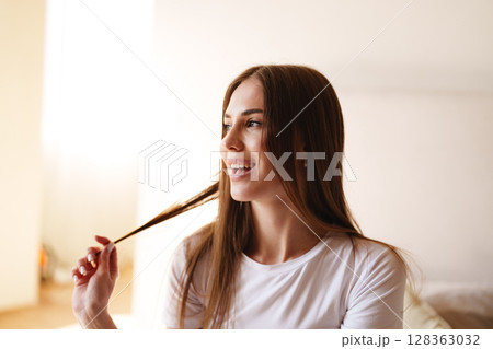 Young woman enjoying a moment of happiness while playing with her hair in a bright indoor setting Young woman enjoying a moment of happiness while playing with her hair in a bright indoor setting 128363032