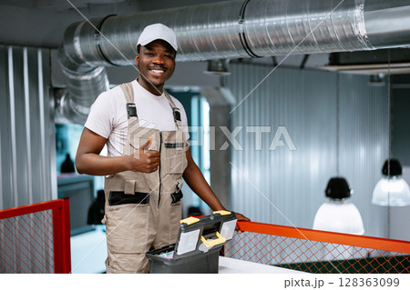 Skilled worker shares a smile while standing next to a toolbox in a modern workspace setting Skilled worker shares a smile while standing next to a toolbox in a modern workspace setting 128363099