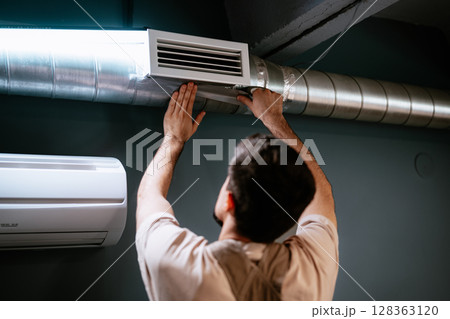 Man servicing air duct in modern interior during home improvement project in the evening 128363120