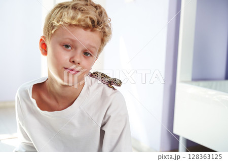Young boy with leopard gecko on shoulder in a bright room during afternoon Young boy with leopard gecko on shoulder in a bright room during afternoon 128363125