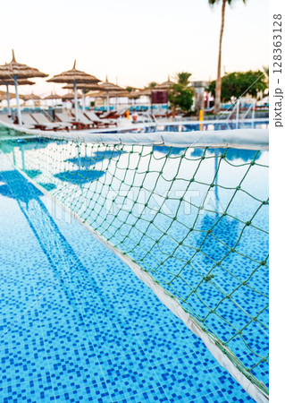 Sunset over a serene swimming pool with clear water and volleyball net in a relaxed resort setting 128363128