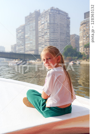 Young girl enjoying a serene moment on a boat in Cairo while gazing at the city skyline 128363132