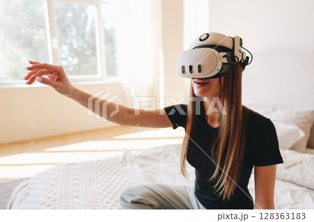 Engaging in an immersive virtual reality experience at home in a cozy bedroom setting Engaging in an immersive virtual reality experience at home in a cozy bedroom setting 128363183