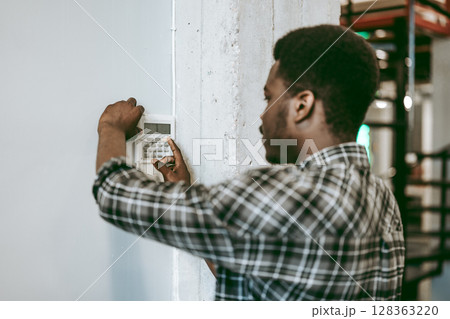 Individual configuring a security system in an industrial workspace during daylight hours Individual configuring a security system in an industrial workspace during daylight hours 128363220