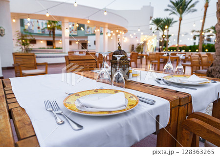 Elegant outdoor dining setup with warm lights and palm trees at a resort restaurant in the evening 128363265