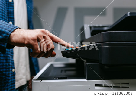 Person operating a copier in an office setting during daylight hours while preparing to make copies of documents 128363303