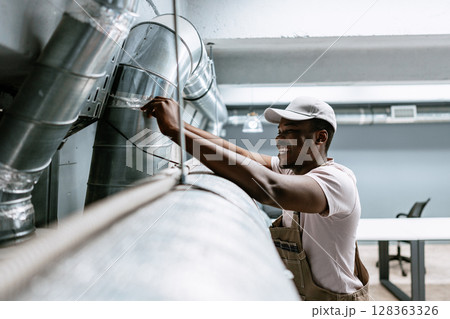 Worker performs maintenance on ductwork in a commercial building during daylight hours Worker performs maintenance on ductwork in a commercial building during daylight hours 128363326