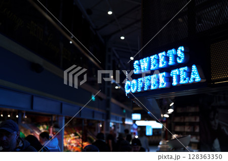 Bright neon sign for coffee and tea shop in bustling market during evening hours 128363350