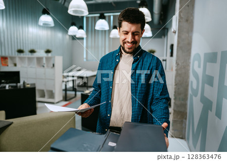 Man smiling while reviewing documents in a modern office setting during daytime 128363476