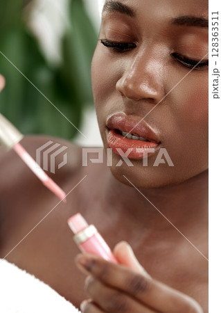 Young woman applying lip gloss in a serene indoor setting surrounded by greenery 128363511