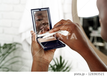 Applying makeup in a bright bathroom with plants, focusing on a mirror reflection in the early morning 128363521