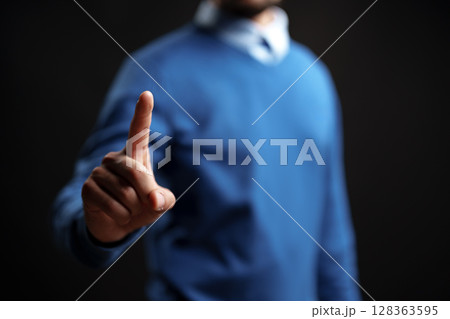 Man signaling to pause with one finger raised, dressed in casual attire against a dark background with soft lighting Man signaling to pause with one finger raised, dressed in casual attire against a dark background with soft lighting 128363595