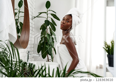 Young woman relaxing in a spa-like bathroom surrounded by greenery after a refreshing shower 128363610
