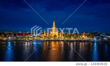 Night view of Wat Arun temple beautifully illuminated on the Chao Phraya River with glowing reflections and city lights in the background Night view of Wat Arun temple beautifully illuminated on the Chao Phraya River with glowing reflections and city lights in the background 128363616