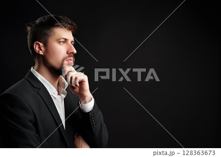 Man in a business suit contemplating ideas against a dark background in a studio setting Man in a business suit contemplating ideas against a dark background in a studio setting 128363673