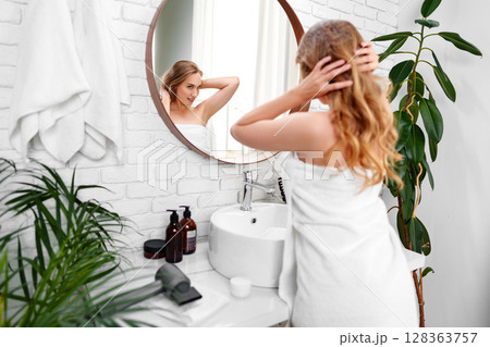 Woman preparing for her day in a stylish bathroom with natural light and green plants Woman preparing for her day in a stylish bathroom with natural light and green plants 128363757